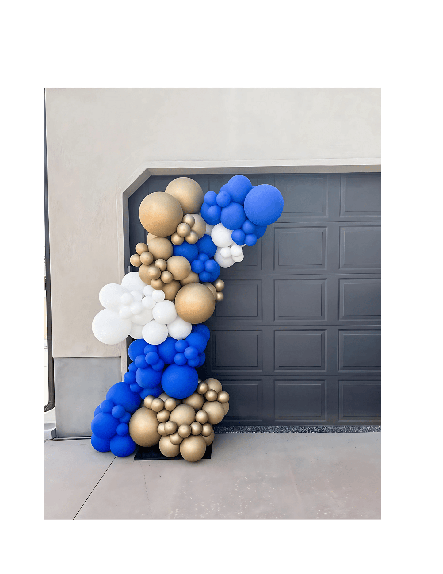 Balloon arch with blue, gold, and white balloons against a garage door.