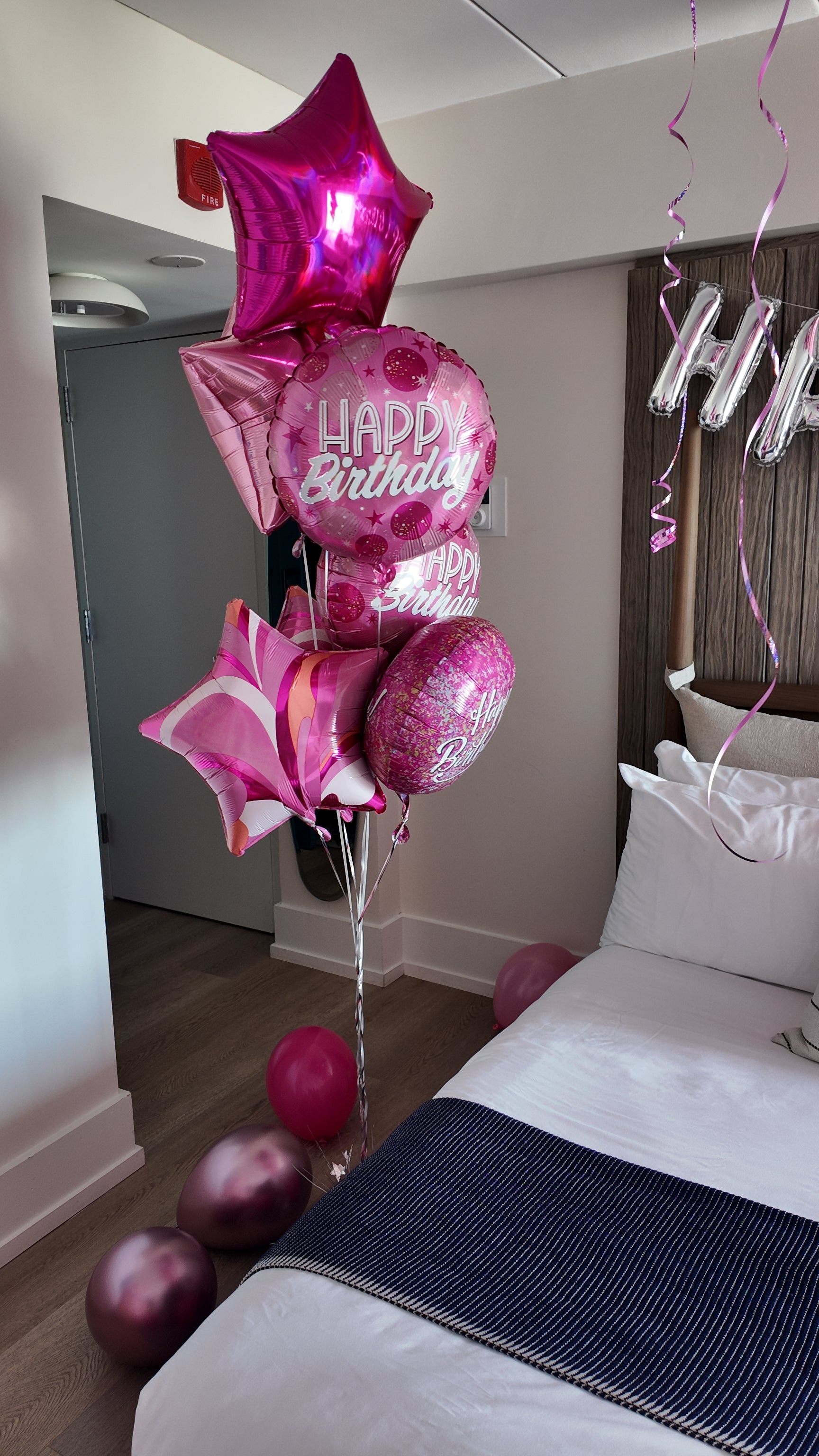 Pink birthday balloons in a room with a bed and decorative streamers.