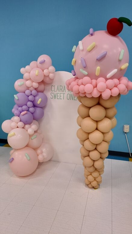 Balloon sculpture of an ice cream cone with a cherry on top against a blue wall.
