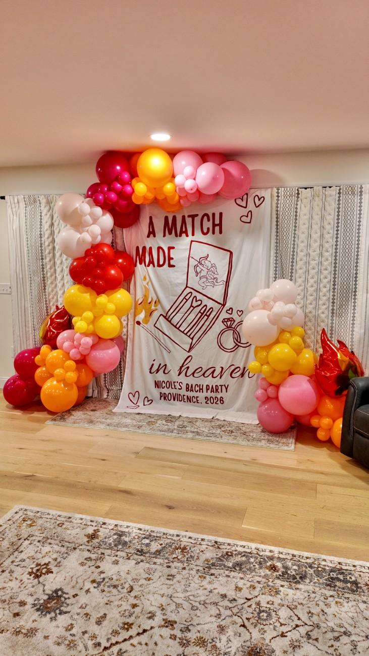 Decorative arch with balloons and a banner on a wooden floor.