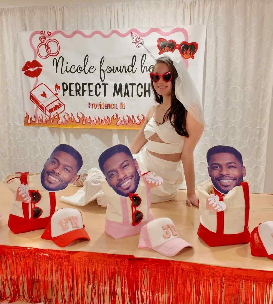 Person in a bridal outfit with 'Perfect Match' backdrop and cutout faces on hats.