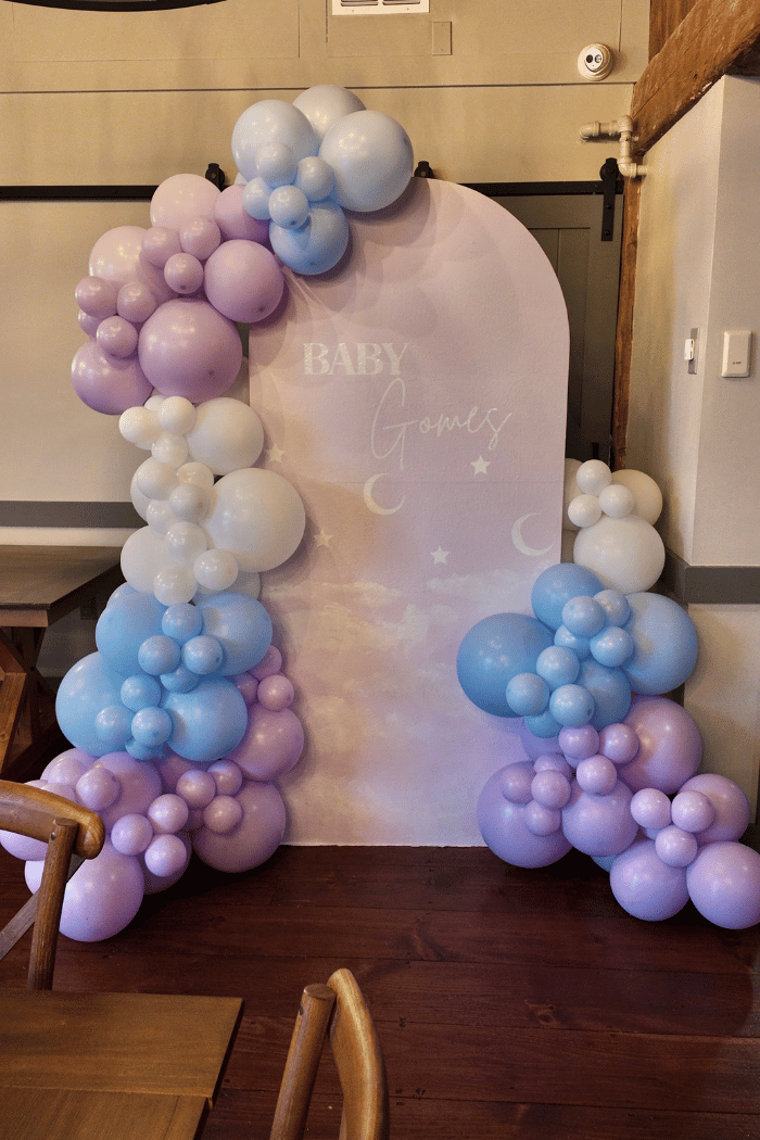 Balloon arch with pastel colors in front of a baby shower backdrop.