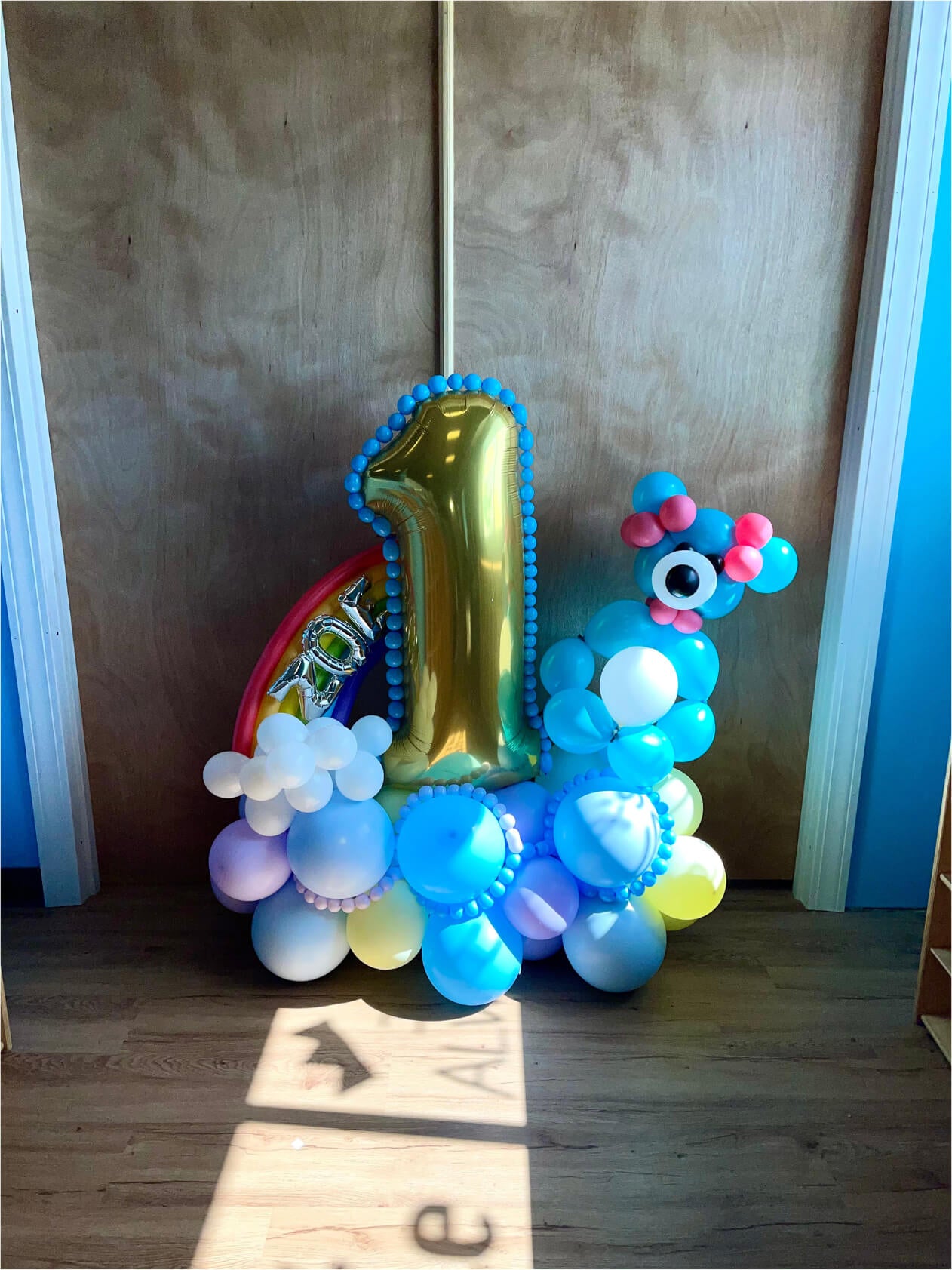 Balloon sculpture of a number '1' with a rainbow and animal-like figure on a wooden floor.
