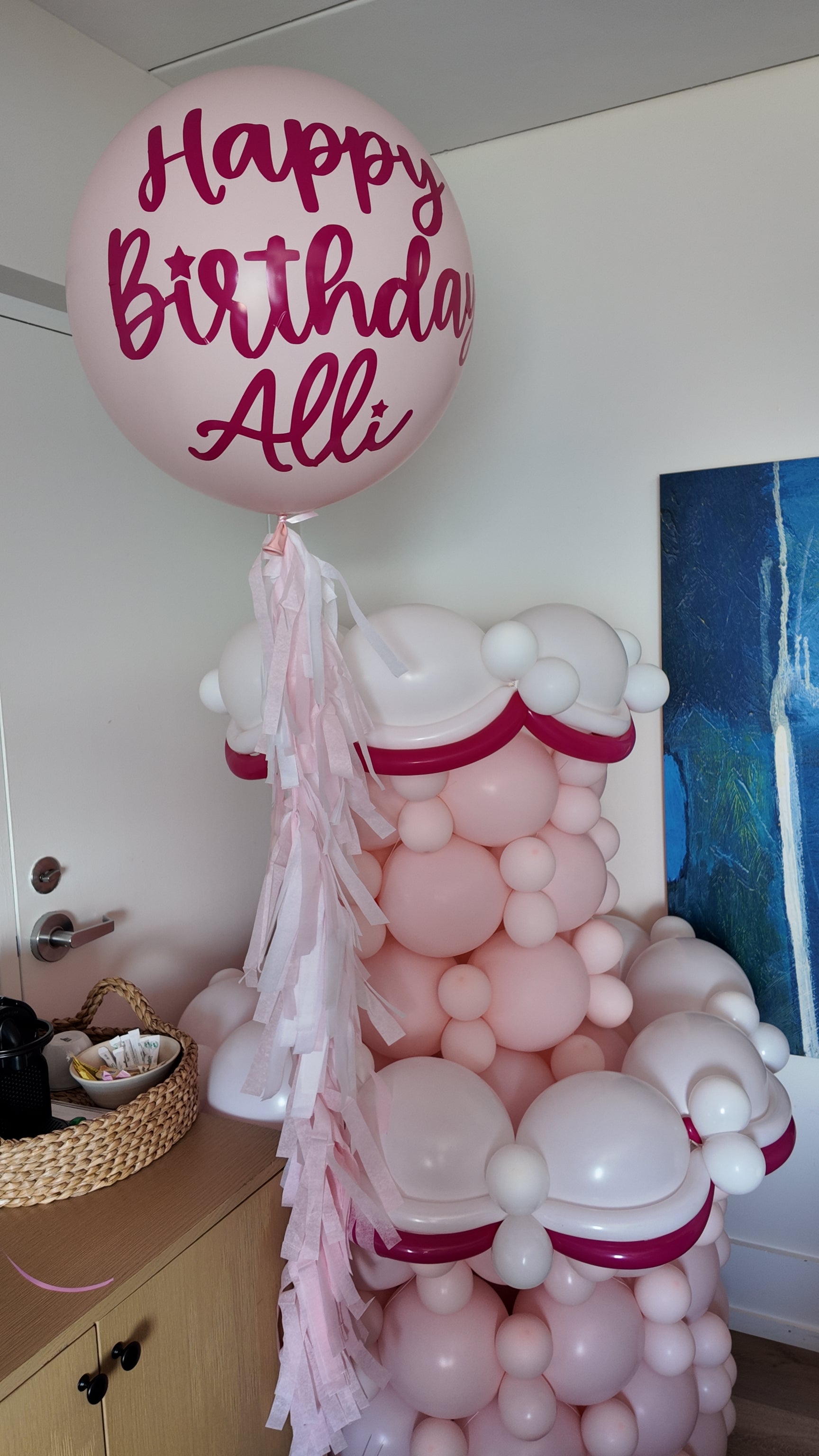 Balloon sculpture with 'Happy Birthday Allie' on a pink balloon in a room.