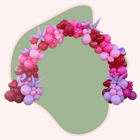 Balloon arch with pink, red, and purple balloons on a green background